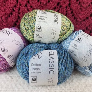 May include: Four skeins of Classic Yarns Cotton Jeans in various colors: purple, green, blue, and light blue. Each skein is labeled as 50g and 75m/82yds, made of 100% cotton. A knitted burgundy fabric is in the background.