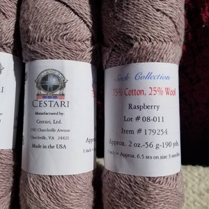 Op de afbeelding: Twee bollen frambooskleurig garen, 75% katoen en 25% wol, met het label "Sock Collection" van Cestari, Ltd. Het label bevat het lotnummer 08-011, artikelnummer 179254 en het garengewicht van 2 ounce, 56 gram en 190 yards.