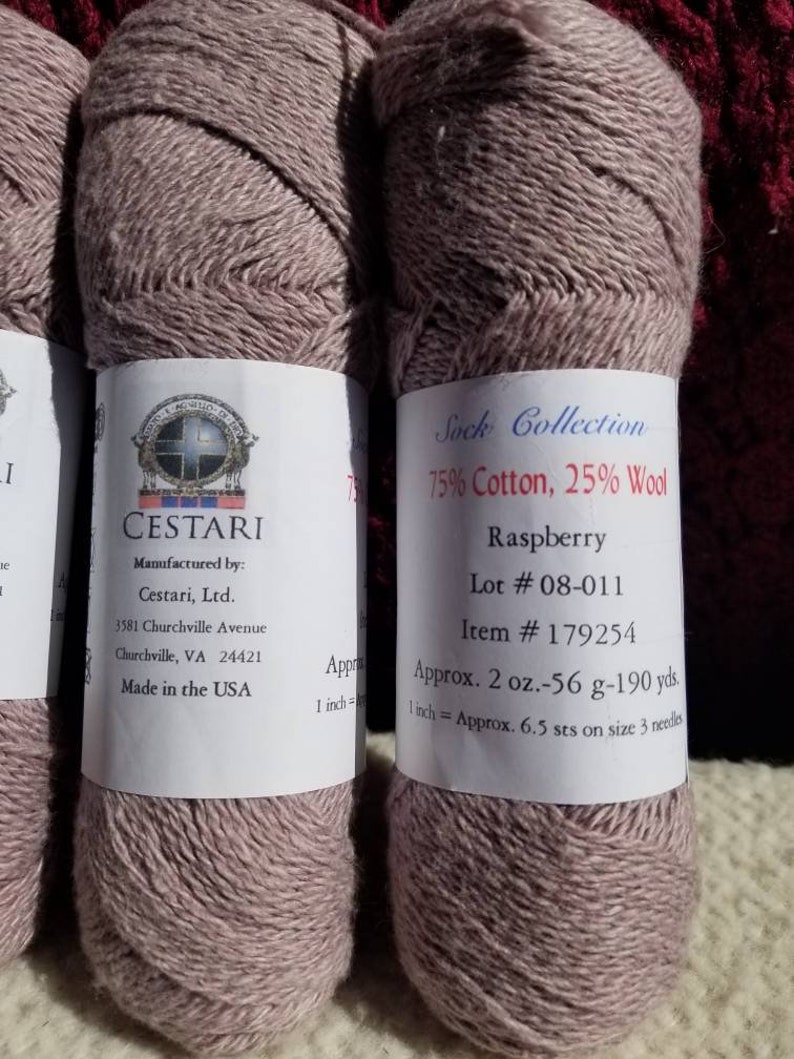 Op de afbeelding: Twee bollen frambooskleurig garen, 75% katoen en 25% wol, met het label "Sock Collection" van Cestari, Ltd. Het label bevat het lotnummer 08-011, artikelnummer 179254 en het garengewicht van 2 ounce, 56 gram en 190 yards.