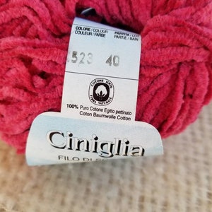 Pu&ograve; includere: Un gomitolo di filato rosa acceso con un'etichetta bianca che recita "COLORE/COLOUR COULUER/FARBE PARTITA/LOT PARTIE/BAIN 1523 40 COTONE 100% FIBRA NATURALE 100% Puro Cotone Egitto pettinato Coton Baumwolle Cotton Ciniglia FILO DI"