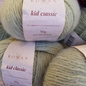May include: Two balls of light green yarn labelled "ROWAN kid classic" with the yarn composition and weight listed on the label.  The yarn is 70% lambswool, 20% kid mohair, and 4% nylon. Each ball weighs 50 grams.