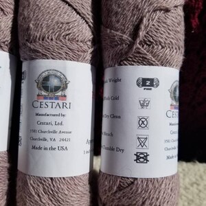 Op de afbeelding: Twee bollen mauve garen met het label "CESTARI" met wasinstructies en de tekst "Manufactured by: Cestari, Ltd. 3581 Churchville Avenue Churchville, VA 24421 Made in the USA".