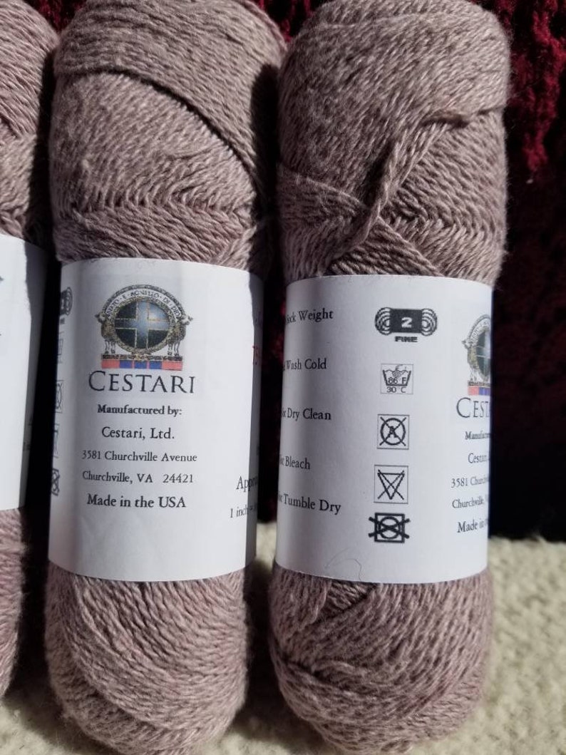 Op de afbeelding: Twee bollen mauve garen met het label "CESTARI" met wasinstructies en de tekst "Manufactured by: Cestari, Ltd. 3581 Churchville Avenue Churchville, VA 24421 Made in the USA".