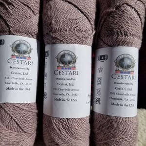 Op de afbeelding: Drie bollen lichtbruin garen met een wit label waarop staat "CESTARI Gemaakt door: Cestari, Ltd. 3581 Churchville Avenue Churchville, VA 24421 Gemaakt in de VS"