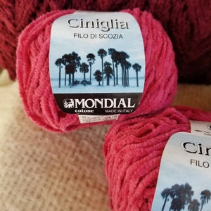 Pu&ograve; includere: Due gomitoli di filato rosa con un'etichetta che recita "Ciniglia FILO DI SCOZIA MONDIAL cotone MADE IN ITALY".