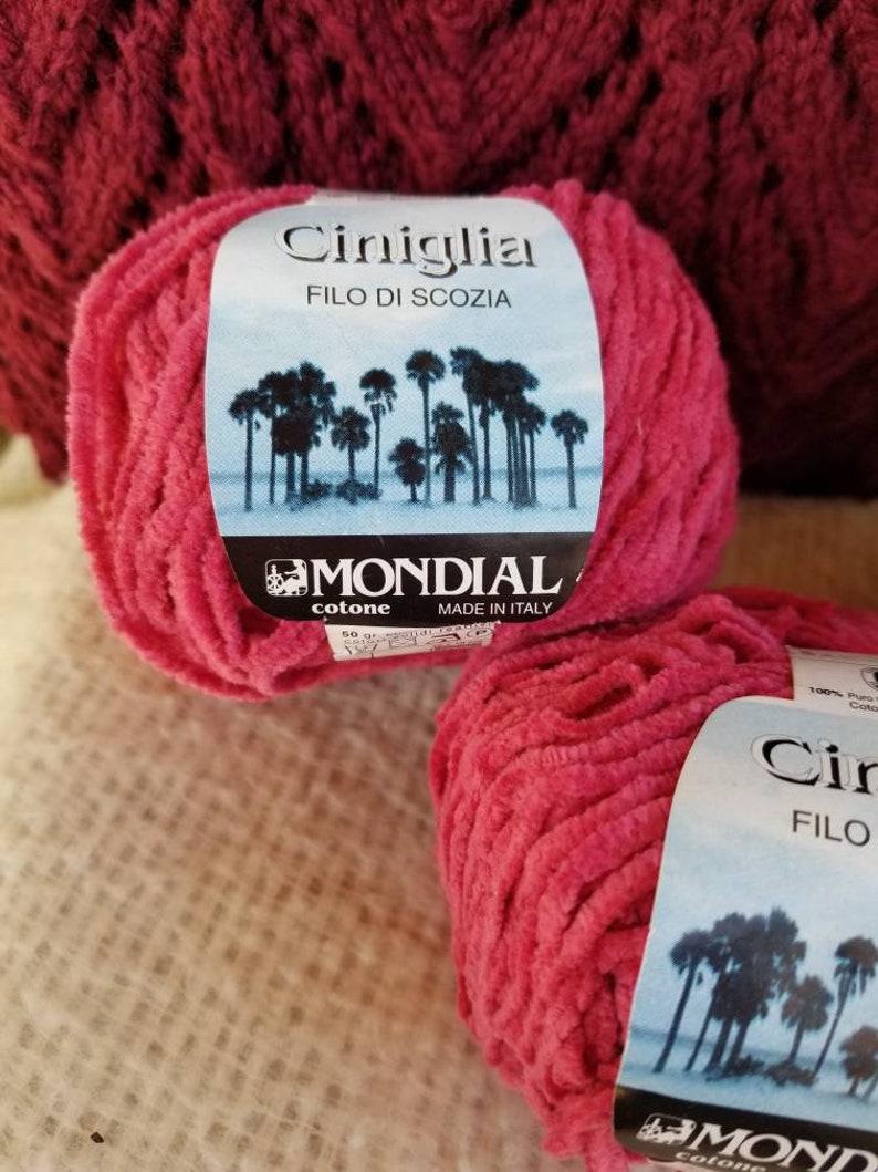 Pu&ograve; includere: Due gomitoli di filato rosa con un'etichetta che recita "Ciniglia FILO DI SCOZIA MONDIAL cotone MADE IN ITALY".