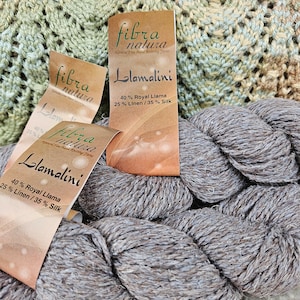 May include: Two skeins of gray yarn labeled "Llamalini" with the text "40% Royal Llama 25% Linen/35% Silk" and "fibra natura Natural Fine Hand Knitting Yarns".