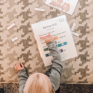 Puede incluir: Un niño está jugando con un juego de aprendizaje colorido que presenta el versículo bíblico Mateo 16:24. El versículo dice: "Entonces Jesús dijo a sus discípulos: Si alguno quiere venir en pos de mí, niéguese a sí mismo, tome su cruz y sígame." El juego incluye cuadrados coloridos con palabras como "tomar" y "tu" que el niño puede hacer coincidir con el versículo.