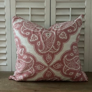 Può includere: Un cuscino decorativo rosa e bianco con un motivo paisley. Il cuscino è appoggiato su una superficie in legno.