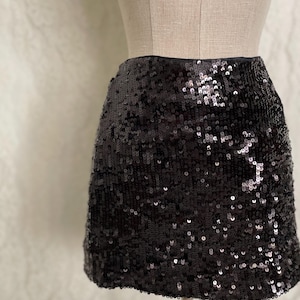 May include: A black sequin mini skirt. The skirt is made of small, shiny sequins and has a fitted silhouette.