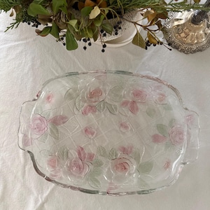 May include: Clear glass serving platter with embossed pink roses and green leaves. The rectangular dish has a lattice pattern and scalloped edges. Decorative floral serving dish.