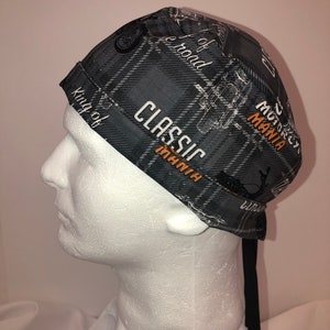 May include: A black and gray plaid motorcycle cap with the words "CLASSIC MANIA" and "MOTORCYCLE MANIA" in white and orange. The cap also has motorcycle illustrations and the words "King of the road".