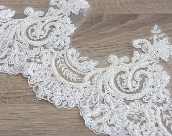 May include: White lace trim with a delicate floral pattern and pearl embellishments. The trim is on a wooden surface.