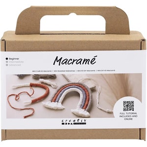 Könnte beinhalten: Ein brauner Karton mit Griff, beschriftet mit "Macramé". Die Box zeigt ein Regenbogen-Makramee-Projekt mit dem Text "Mini Craft Kit Macramé". Das Set enthält Materialien und einen QR-Code für ein vollständiges Tutorial.