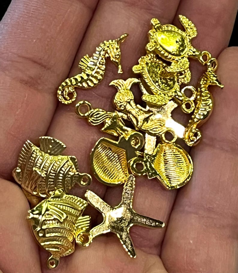 May include: A collection of gold-colored charms in various sea life shapes, including seahorses, fish, starfish, and shells. Each charm has a small loop for attaching to jewelry or other crafts. The charms are highly detailed and have a shiny finish.