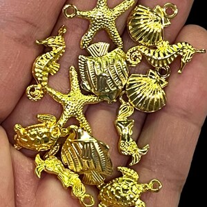 May include: A collection of gold-colored charms in various sea-themed shapes, including starfish, seahorses, fish, turtles, and seashells. The charms are detailed and have small loops for attaching to jewelry or other crafts.