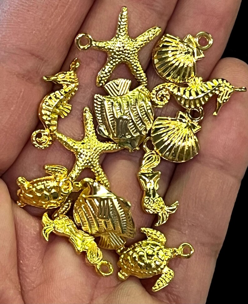 May include: A collection of gold-colored charms in various sea-themed shapes, including starfish, seahorses, fish, turtles, and seashells. The charms are detailed and have small loops for attaching to jewelry or other crafts.