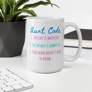 Könnte beinhalten: Eine weiße Keramik-Kaffeetasse mit einem blauen und rosa Design, auf der "Aunt Code" steht und drei Regeln aufgelistet sind: "1. Schlafenszeit ist, wann immer. 2. Die Antwort ist immer ja. 3. Deine Mutter muss es nicht wissen."