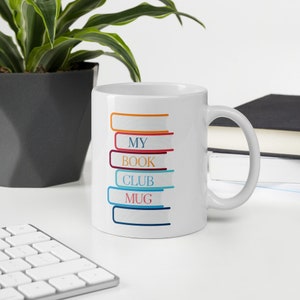 May include: White ceramic mug with a colorful graphic of stacked books that reads "My Book Club Mug".