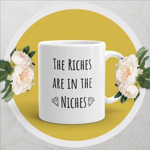 Puede incluir: Taza de cerámica blanca con texto negro que dice "The Riches Are In The Niches" con un símbolo de diamante a cada lado de la palabra "Niches".