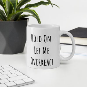 May include: White ceramic mug with black text that reads "Hold on Let me Overreact".