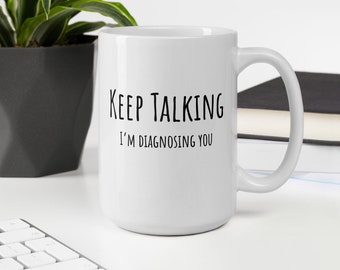 May include: White ceramic coffee mug with black text that reads "Keep Talking I'm Diagnosing You".