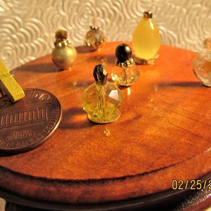 May include: A collection of miniature glass perfume bottles in various colors and styles, including clear, yellow, and gold, arranged on a wooden table top with a penny.