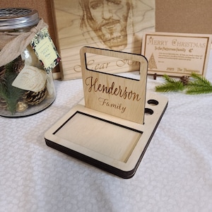 May include: A wooden desk organizer with a slot for a phone or tablet, a pen holder, and a small shelf. The organizer is personalized with the text "Henderson Family".