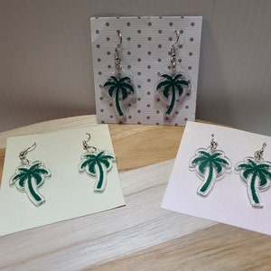 May include: Three pairs of green palm tree earrings on display cards. The earrings are made of clear acrylic with a green palm tree design.