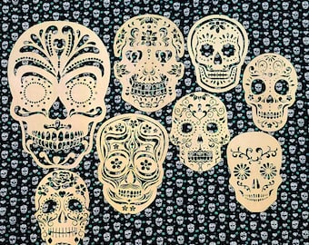 May include: A set of ten decorative sugar skull cutouts, each with a unique design. The skulls are white with black details and are arranged in a pattern on a black and white background.