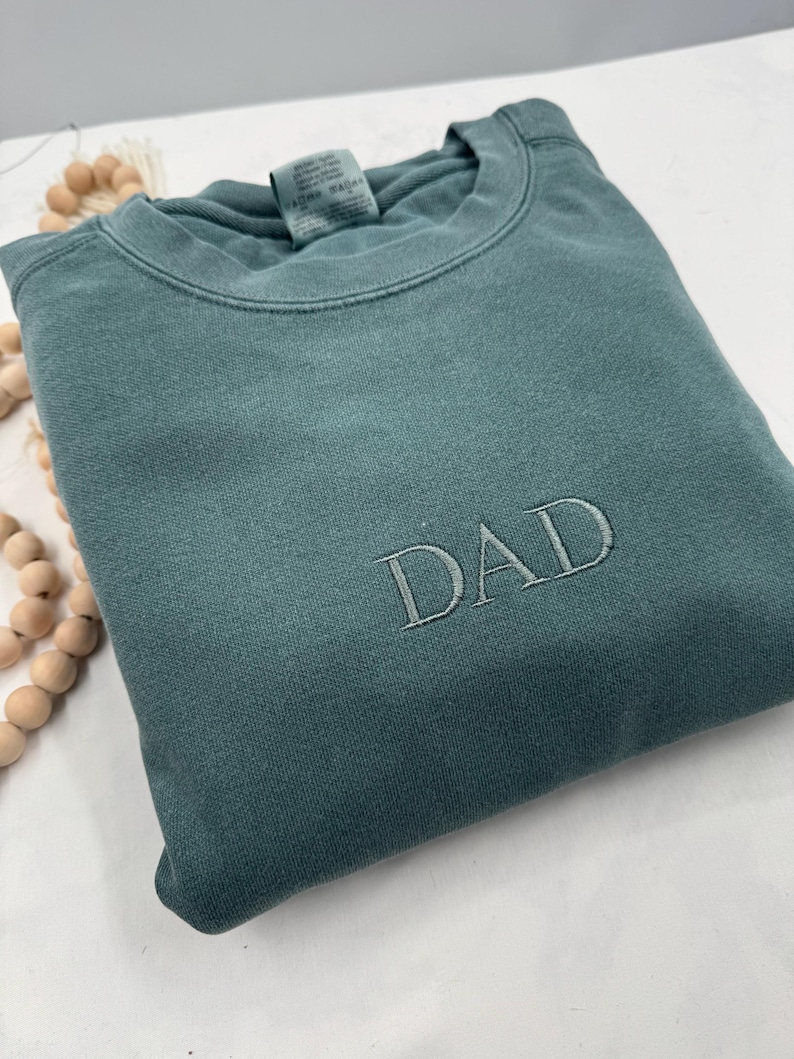 May include: A teal blue sweatshirt with the word "DAD" embroidered in white on the front.
