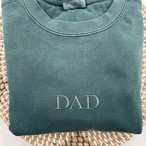 May include: A dark green sweatshirt with the word "DAD" embroidered on the front.