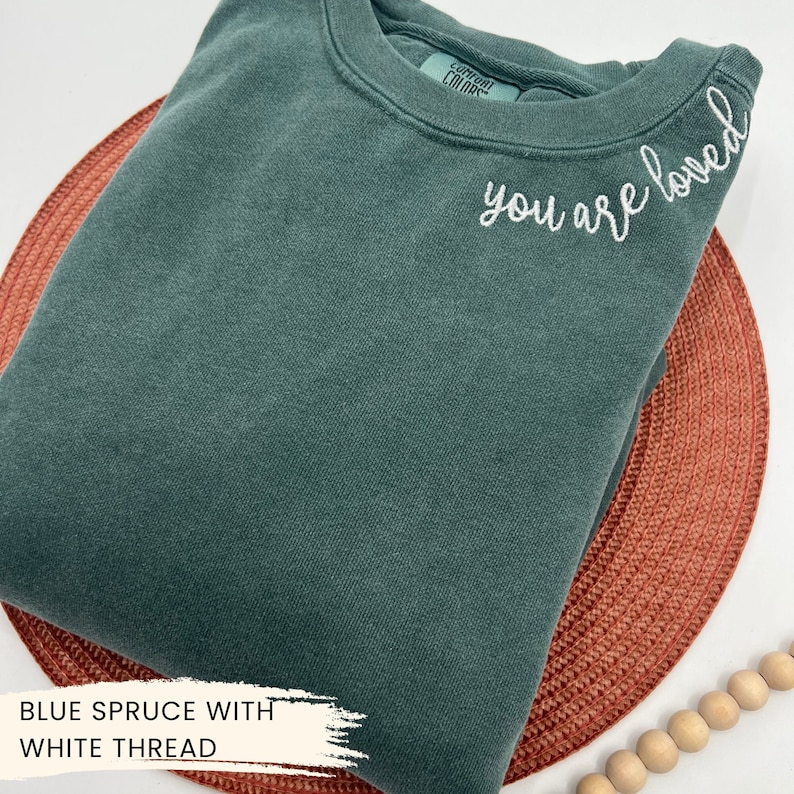 May include: A blue spruce coloured sweatshirt with the text "you are loved" embroidered in white thread.