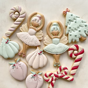Può includere: Un assortimento di biscotti di zucchero decorati in varie forme. I biscotti includono ballerine, bastoncini di zucchero, alberi di Natale e forme di pesca, tutti con dettagli di glassa intricati. La tavolozza dei colori è tenue, con pastelli e bianco.