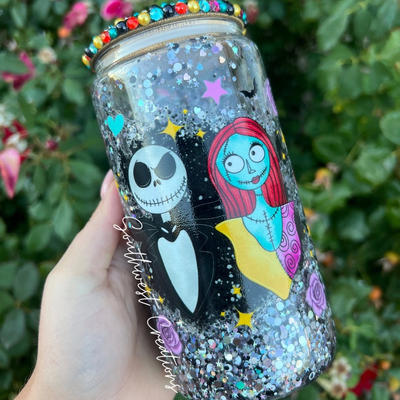 Puede incluir: Un vaso de glitter negro y plateado con una tapa de cuentas de colores. El vaso presenta un gr&aacute;fico de Jack Skellington y Sally de Pesadilla antes de Navidad.