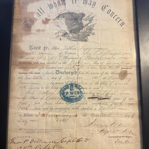 Può includere: Documento antico incorniciato con una scrittura ornata e un'aquila. Il documento, datato 1863, sembra essere un documento di congedo dell'esercito americano. Il testo include dettagli sul servizio di un soldato, la sua descrizione fisica e la sua firma.