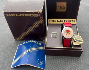 May include: Vintage Helbros watch in its original box. The watch has a red band and a white face with a cartoon character. The box is brown with gold lettering and the Helbros logo. A blue pamphlet is also included.