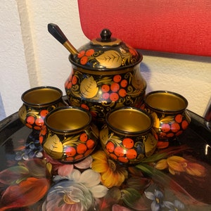 Pode incluir: Um conjunto de bonecas russas de encaixe, ou bonecas matrioska, com fundo preto e desenhos florais vermelhos e dourados. O conjunto inclui uma boneca grande com tampa e quatro bonecas menores.