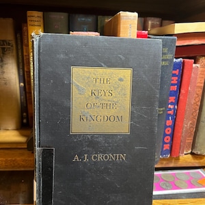 May include: A black hardcover book titled "The Keys of the Kingdom" by A. J. Cronin. The book is on a bookshelf with other books.