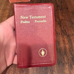 May include: A red leather-bound book with the title "New Testament Psalms Proverbs" in gold lettering. A gold symbol of a chalice with a flame is on the front cover.