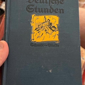 May include: A vintage book titled "Deutsche Stunden" with a dark blue cover and gold trim. The cover features a gold illustration of a castle on a mountain and the name "Schmidt-Glotte".