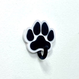 May include: White paw print shaped hook with a black paw print design. The hook is designed to hang items on a wall.