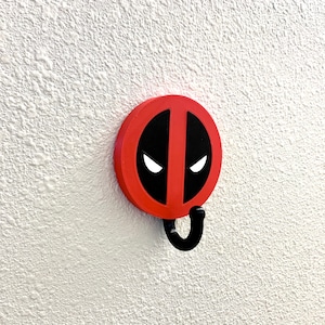 May include: Red and black wall hook shaped like Deadpool's mask with a black hook.