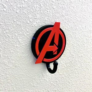 May include: A black and red wall hook shaped like the Avengers logo. The hook is a circle with a red "A" inside.