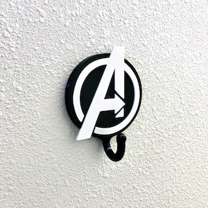 May include: A black and white Avengers logo wall hook with a hook shaped like an arrow. The logo is a circle with a white letter A inside.