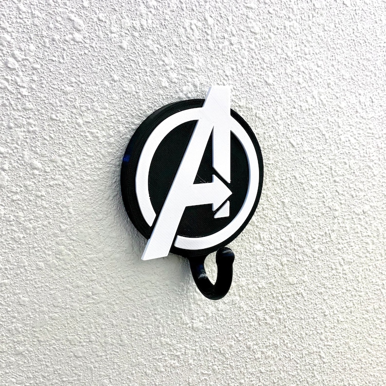 May include: A black and white Avengers logo wall hook with a hook shaped like an arrow. The logo is a circle with a white letter A inside.