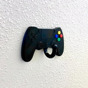 May include: A black plastic video game controller shaped wall hook with a hook on the bottom. The controller has four colored buttons: red, yellow, blue, and green.