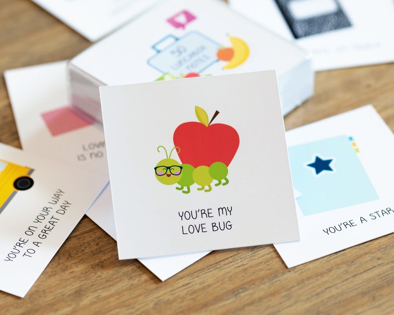 May include: A white card with a green worm wearing glasses and a red apple on top. The text on the card reads "You're my love bug."