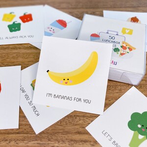 May include: A set of 50 cards with cute food illustrations and puns. The cards feature a banana, a broccoli, a pepper, a french fry, and a loaf of bread. The text on the cards includes phrases like "I'm bananas for you" and "Let's broc-oli!"
