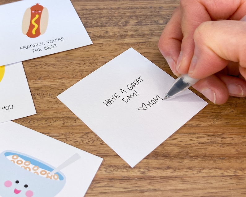 May include: White card with the handwritten message "Have a great day!" and a heart with "Mom" written below it.